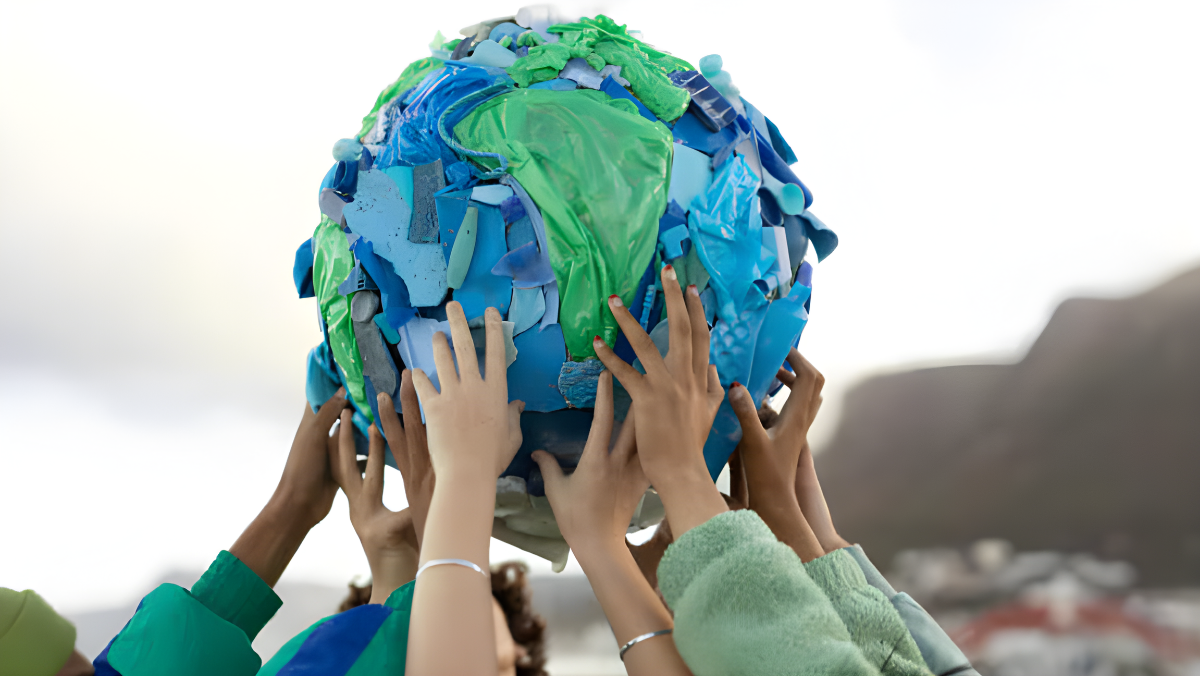 Hands lifting a model Earth made of recycled blue and green plastic pieces.