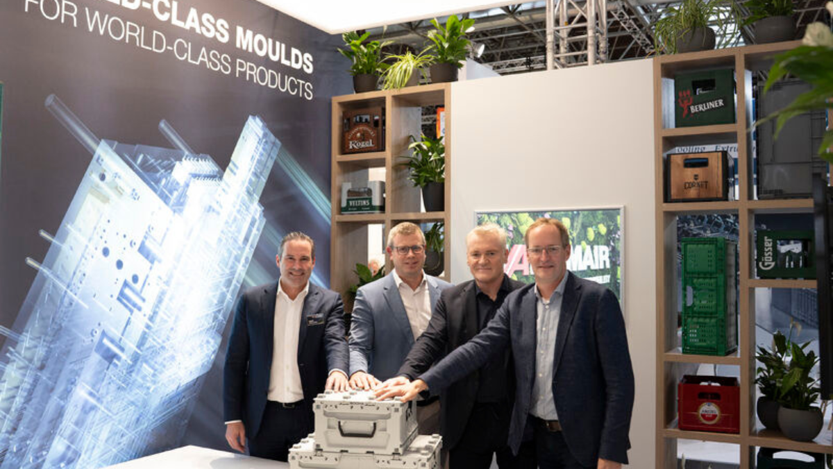 Executives standing together with hands on plastic moulding crates at event booth